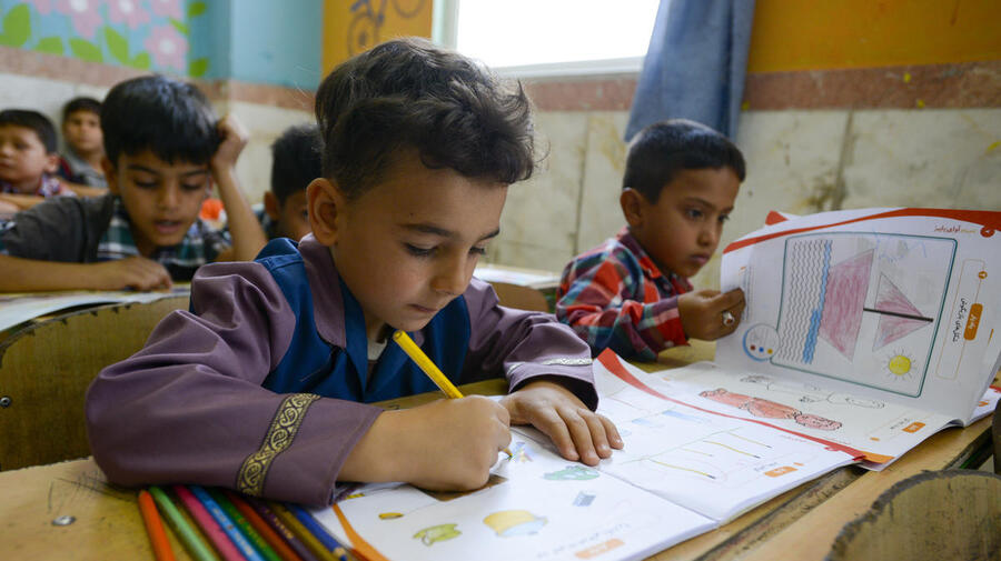 Boy writing in a workbook at a classroom desk