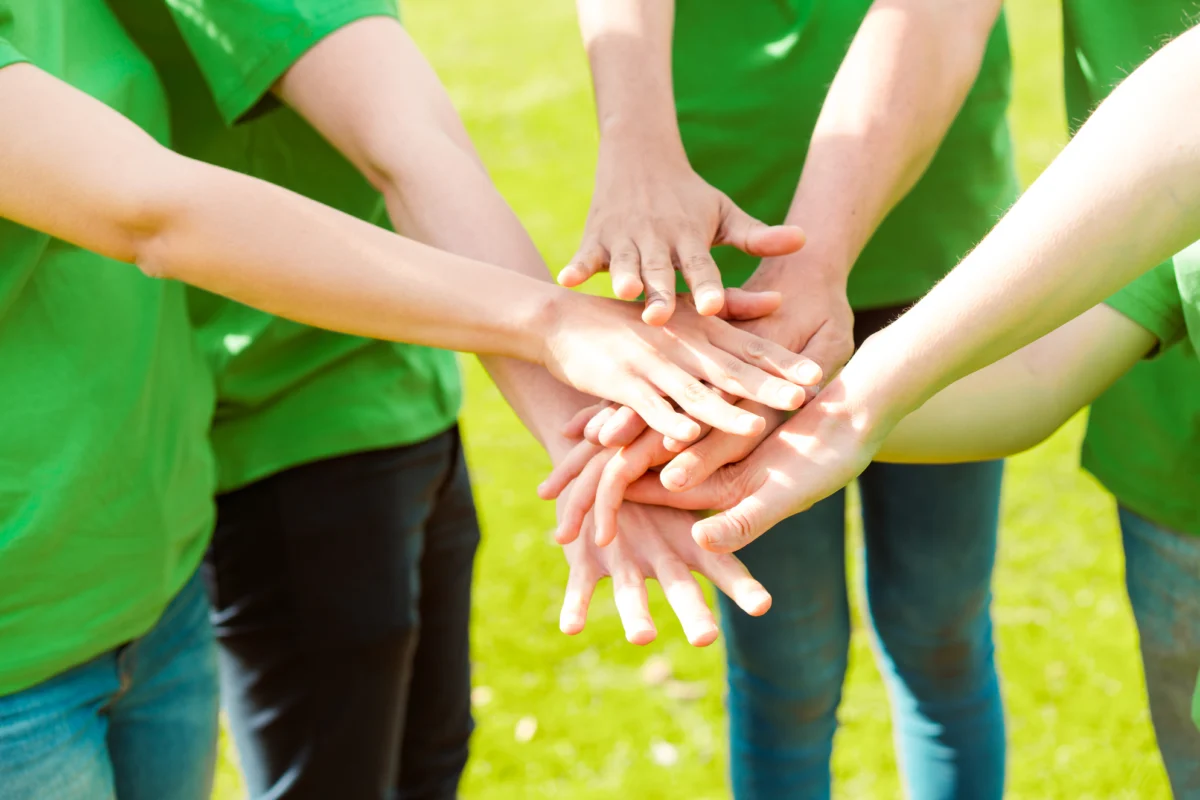 Volunteers in green shirts stacking their hands together